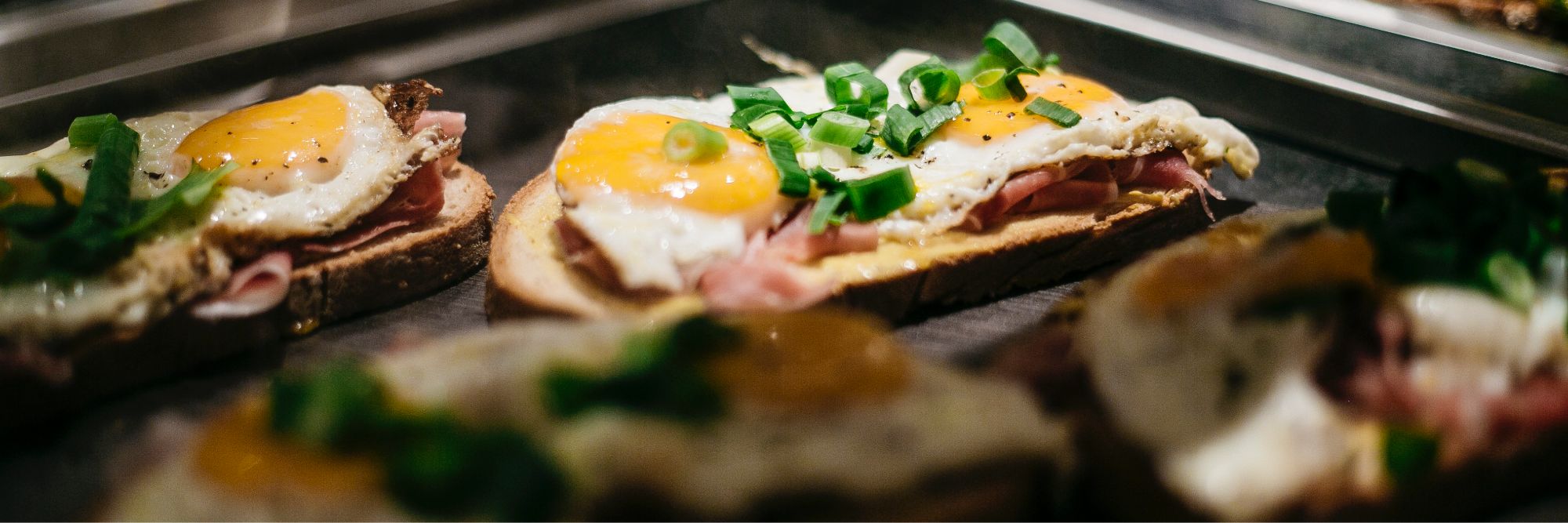 Nahaufnahme eines belegten Brotes mit Spiegelei, Bacon und Frühlingszweibeln